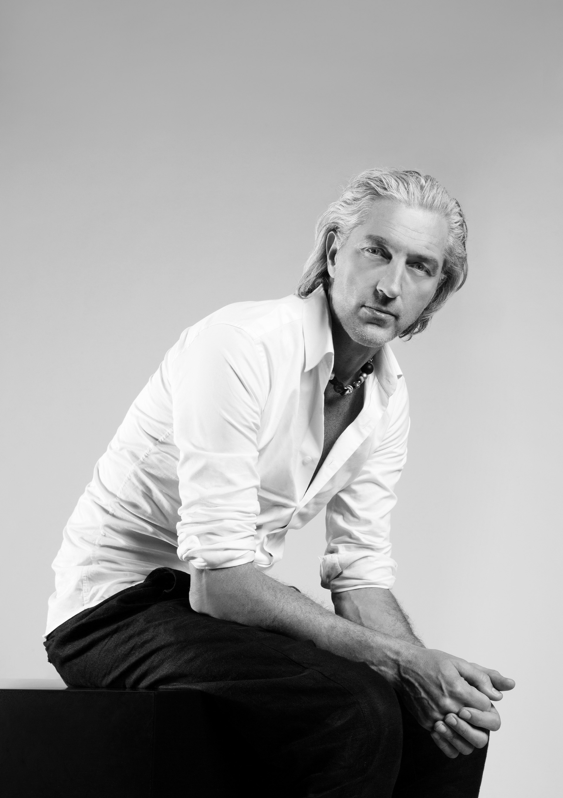 Marcel Wanders s'assoit et regarde directement dans l'appareil photo avec les mains jointes.